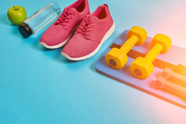 Healthy concept, diet plan with sport shoes and bottle of water and dumbbells on blue background, healthy food and exercise concept. Sun flare