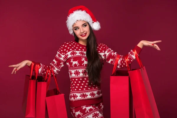 Młoda ładna kobieta lub dziewczyna z długo piękne włosy w Santa hat i nowy rok ubierać, trzymając czerwony pakiet na tle czerwony studio — Zdjęcie stockowe