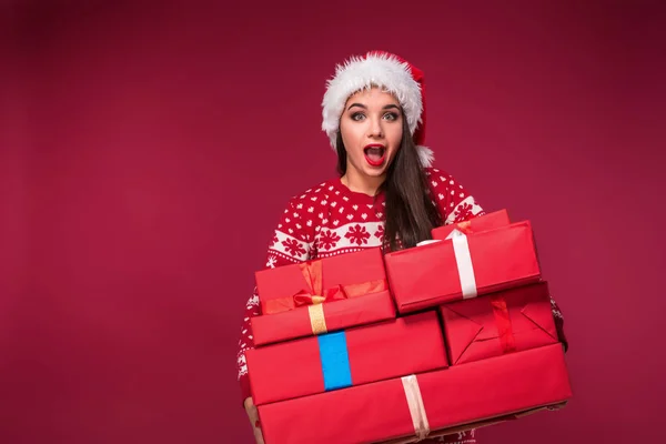 Młoda kobieta w sweter i Boże Narodzenie kapelusz gospodarstwa pudełeczka i patrząc na kamery na czerwonym tle — Zdjęcie stockowe