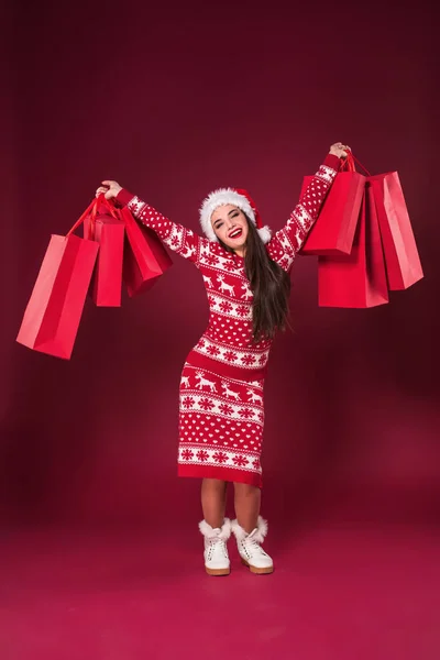 Młoda ładna kobieta lub dziewczyna z długo piękne włosy w Santa hat i nowy rok ubierać, trzymając pakiet czerwony czerwony studio tło. Album zdjęć — Zdjęcie stockowe