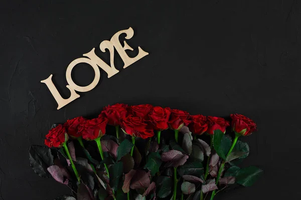 Punaiset ruusut kukkia puinen sana LOVE mustalla taustalla — kuvapankkivalokuva