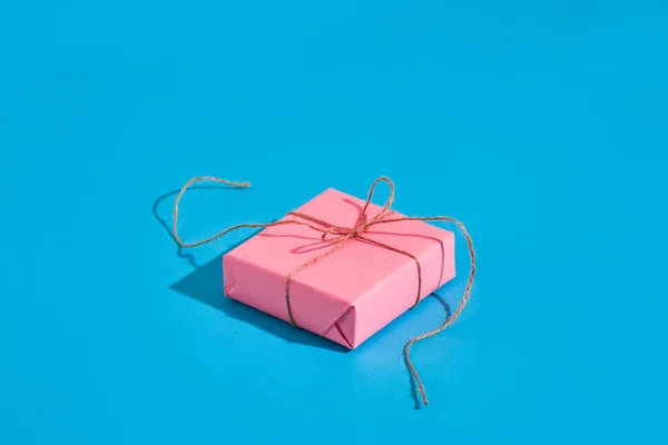 Rosa presentförpackning med tunn bundet rep med skugga på blå bakgrund — Stockfoto
