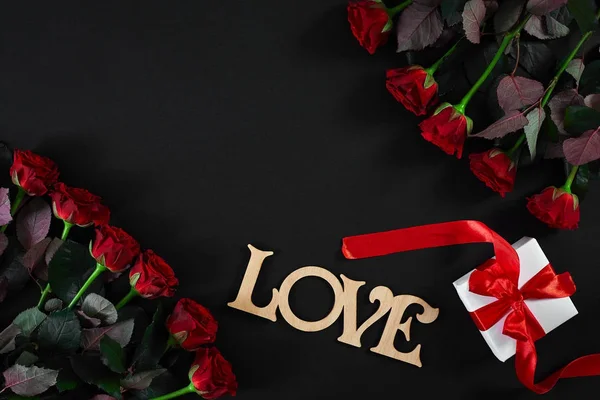 Λουλούδια κόκκινα τριαντάφυλλα με ξύλινη λέξη Love σε μαύρο φόντο με — Φωτογραφία Αρχείου