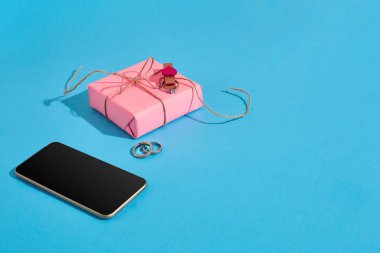 Alyans ve pembe hediye kutusu mavi arka plan ve telefon. Evlenme teklifi. Sevgililer günü kavramı