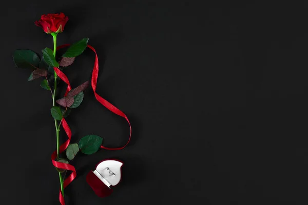 Una rosa roja oscura con cinta roja y caja con anillo en bac negro — Foto de Stock