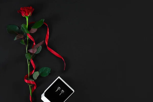 Una rosa roja oscura con cinta roja y caja con pendientes en negro — Foto de Stock