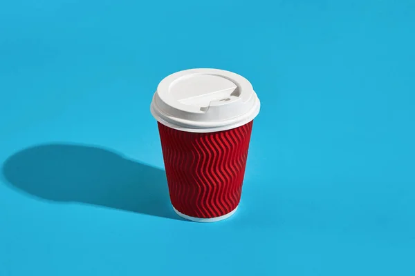 Hot coffee in red paper cup with white lid on blue background wi