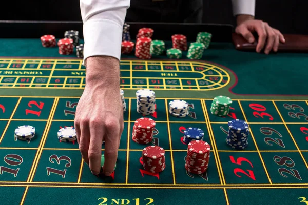 Крупним планом яскраве зображення зеленого столу казино з рулеткою, з руками крутіших і різнокольорових чіпсів . — стокове фото