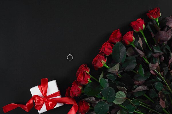 Красные розы, кольцо и подарочная коробка на черном фоне
