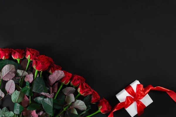 Rode rozen en witte geschenkdoos met rood lint op zwarte achtergrond — Stockfoto