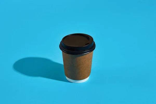 Café caliente en taza de papel marrón con tapa negra sobre fondo azul — Foto de Stock