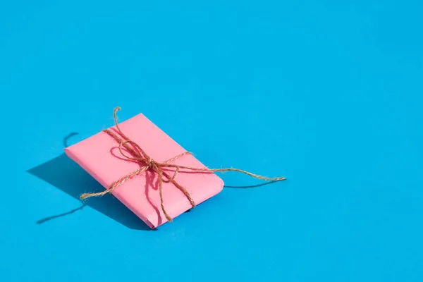 Rosa presentförpackning med tunn bundet rep med skugga på blå bakgrund — Stockfoto