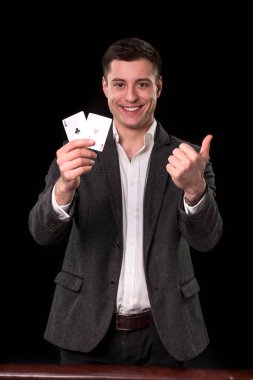 İki as elinde tutan ve gülümseme ile el hareketi yukarı siyah arka plan üzerinde gösterilen takım elbise Beyaz delikanlı. Kumar kavramı. Casino