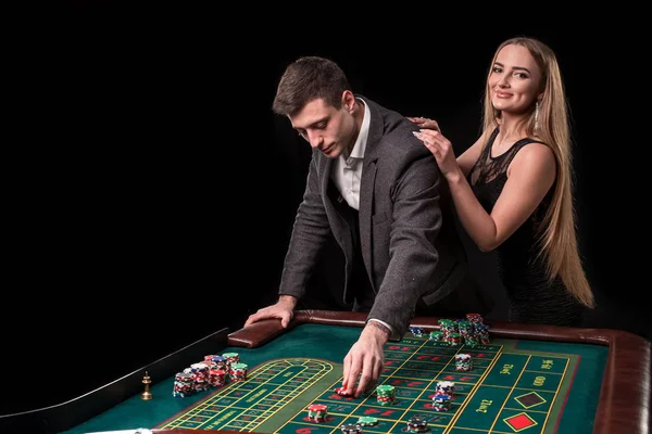 Elegantes Paar im Casino, das auf dem Roulette wettet, auf schwarzem Hintergrund — Stockfoto