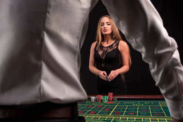 Detail na zadní straně krupiér v bílé tričko, obrázek zelené kasino tabulky s ruletou a čipy, bohatá žena sázení hazardu v pozadí — Stock fotografie