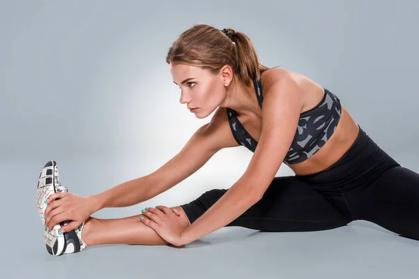 Stretching-Trainingshaltung einer Frau auf grauem Studiohintergrund — Stockfoto