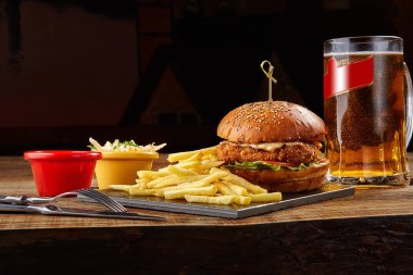 Lezzetli burger, patates kızartması sosu ve bardak bira kara tahta üzerinde