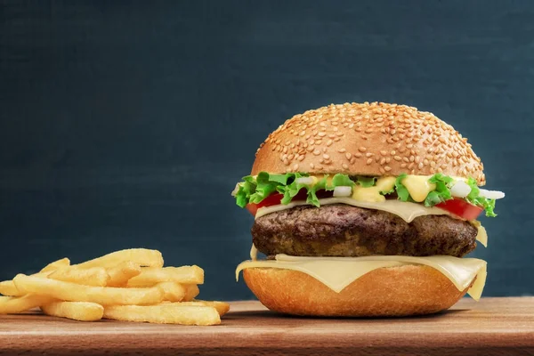 Fast food. Cheeseburger and french fries on a wooden board, on dark background — Stock Photo, Image