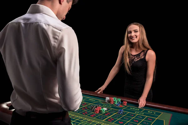 Un primer plano en la parte posterior del crupier en una camisa blanca, imagen de la mesa de casino verde con ruleta y fichas, una mujer rica apostando de juego en el fondo — Foto de Stock