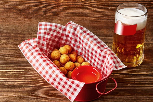 Hot cheese balls with sauce and glass of beer on wooden table
