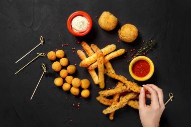 Mantar meyilli, peynir topları, peynirli çubuk ve vurucu, otlar, sos, ketçap ve biber ile siyah arka plan üzerine peynir halkaları. Üstten Görünüm