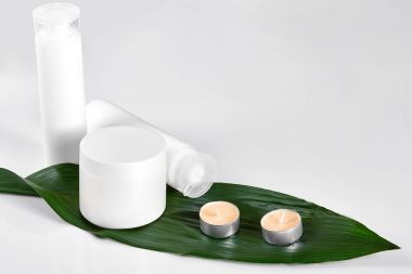 Beyaz kozmetik ürünler ve beyaz zemin üzerine yeşil yaprak. Mock-up kavramı için doğal güzellik ürünleri.