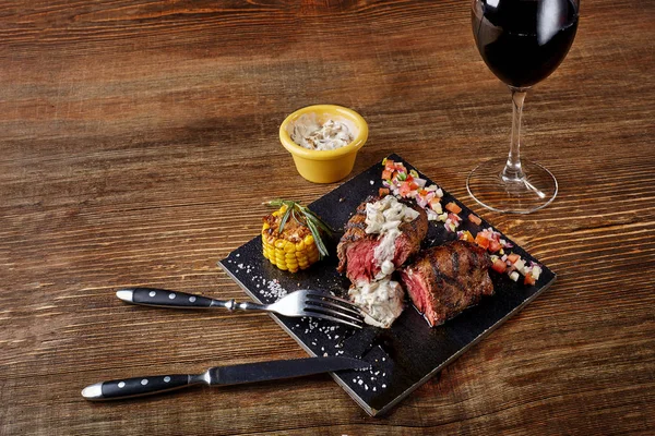Barbecue steak with a glass of red wine as close-up on black board on wooden background — Stock Photo, Image