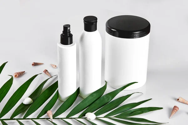 Productos cosméticos blancos y hojas verdes sobre fondo blanco. Productos de belleza natural para el concepto de maqueta de branding . — Foto de Stock