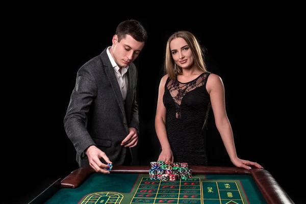 Elegante pareja en el casino apostando por la ruleta, sobre un fondo negro — Foto de Stock