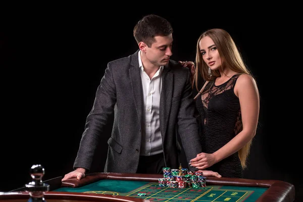 Elegante pareja en el casino apostando por la ruleta, sobre un fondo negro — Foto de Stock