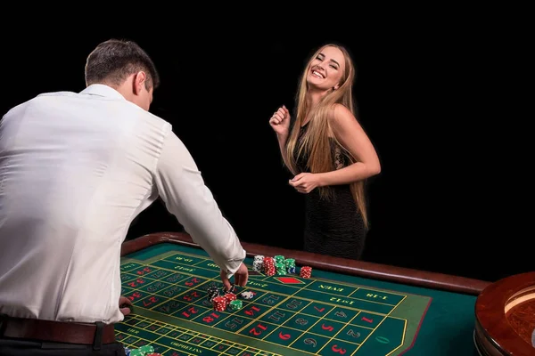 Um close-up na parte de trás do croupier em uma camisa branca, imagem de mesa de casino verde com roleta e fichas, uma mulher rica apostando de jogos de azar no fundo — Fotografia de Stock