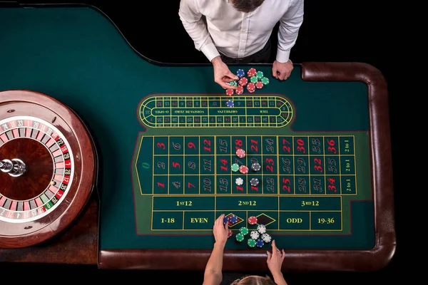 Чоловік крутіший і жінка грає в рулетку за столом в казино. Вид зверху на зелений стіл рулетки зі стрічкою . — стокове фото