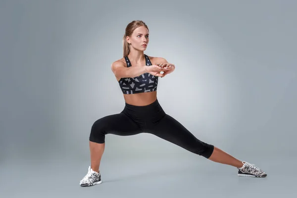 Stretching workout posture by a woman on studio gray background — Stock Photo, Image