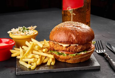 Lezzetli burger, patates kızartması sosu ve bardak bira kara tahta üzerinde