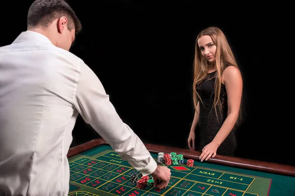 En närbild på baksidan av croupier i en vit skjorta, bilden av gröna casino bord med roulette och chips, en rik kvinna vadslagning av hasardspel i bakgrunden — Stockfoto