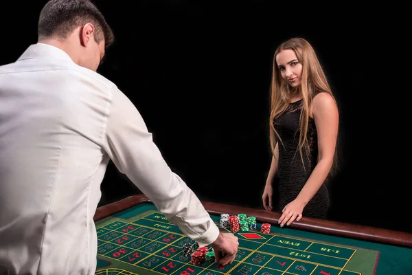 Un primer plano en la parte posterior del crupier en una camisa blanca, imagen de la mesa de casino verde con ruleta y fichas, una mujer rica apostando de juego en el fondo —  Fotos de Stock