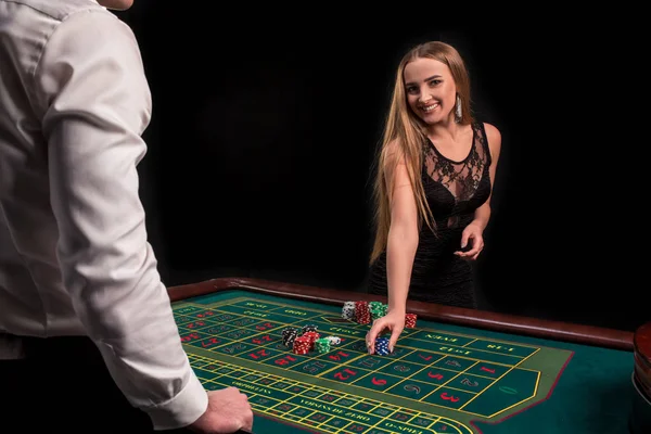 Un primer plano en la parte posterior del crupier en una camisa blanca, imagen de la mesa de casino verde con ruleta y fichas, una mujer rica apostando de juego en el fondo — Foto de Stock