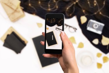 El ile bir smartphone fotoğraf çalışma alanını defter, kahve fincanı, eşarp, gözlük ile yapar.