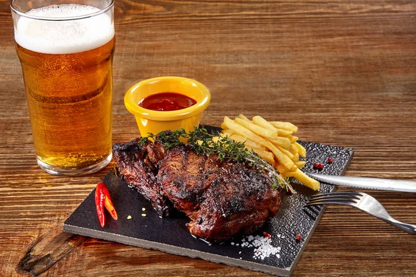 Glas Bier mit Gourmet-Steak und Pommes auf Holzgrund. — Stockfoto