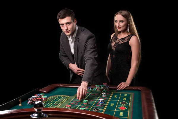 Élégant couple au casino pariant sur la roulette, sur fond noir — Photo