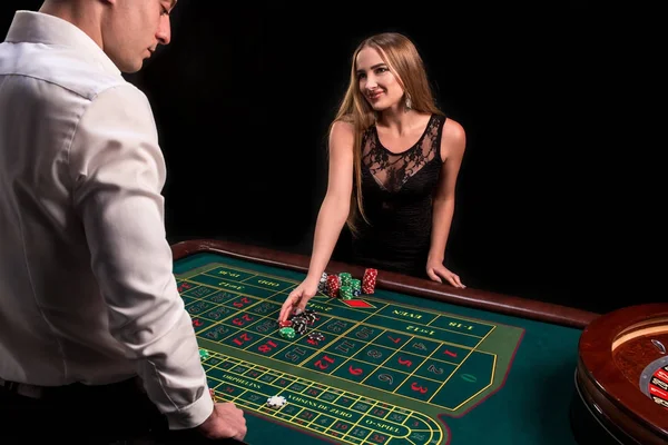 Un primer plano en la parte posterior del crupier en una camisa blanca, imagen de la mesa de casino verde con ruleta y fichas, una mujer rica apostando de juego en el fondo — Foto de Stock