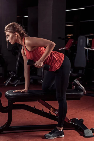 Giovane bella ragazza bionda è impegnata in allenamento sportivo con i manubri in palestra — Foto Stock