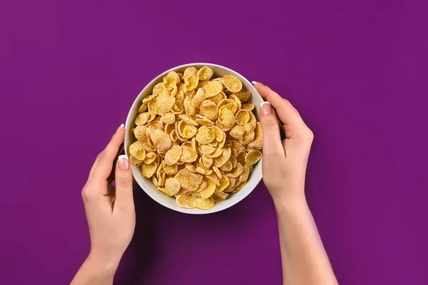 Женские руки держат миску со здоровым завтраком, крупным планом. Чаша с кукурузными хлопьями на красочном фоне — стоковое фото