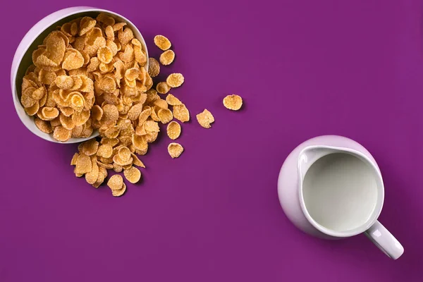 Cuenco con hojuelas de maíz, jarra de leche sobre fondo púrpura, vista superior —  Fotos de Stock