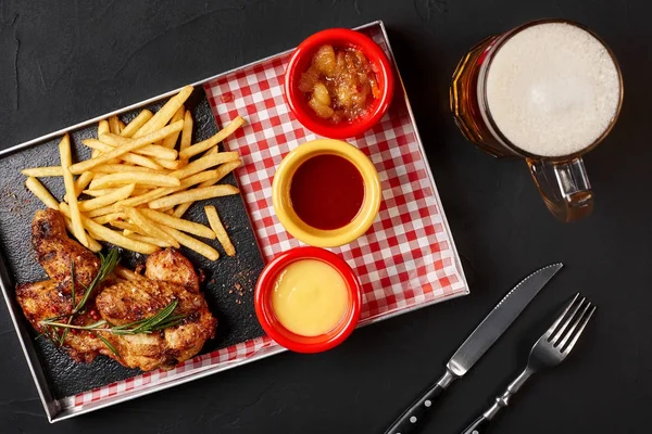 Gebackene Chicken Wings mit Pommes frites auf einem eisernen Tablett mit einem Glas Bier auf schwarzem Hintergrund — Stockfoto