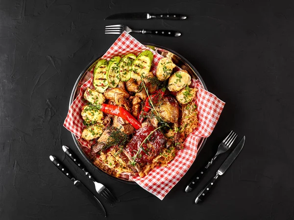 Verschiedene köstliche Grillfleisch mit Gemüse und BBQ-Sauce auf einem eisernen Tablett auf schwarzem Hintergrund in Großaufnahme. große Auswahl an warmen Fleischgerichten. Ansicht von oben — Stockfoto