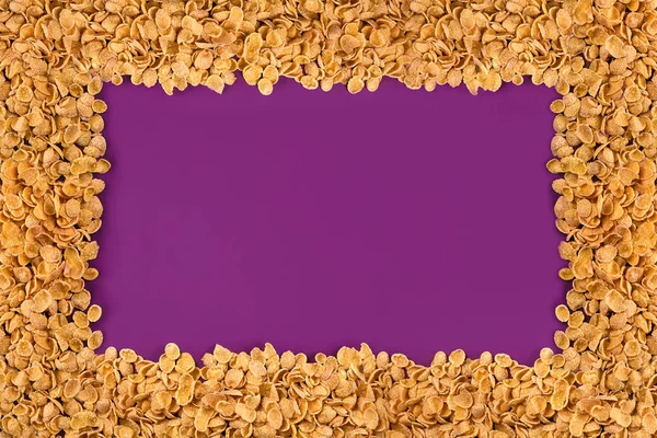 En ram fodrad med cornflakes. Cornflakes utspridda på en lila bakgrund. Kopiera utrymme — Stockfoto