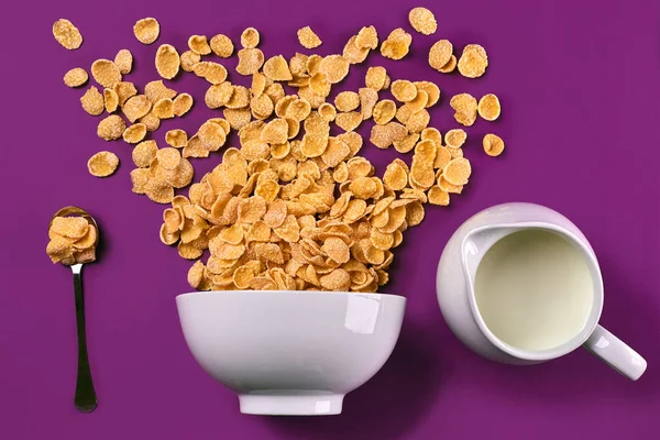 Cuenco con hojuelas de maíz, jarra de leche y cuchara sobre fondo púrpura, vista superior —  Fotos de Stock