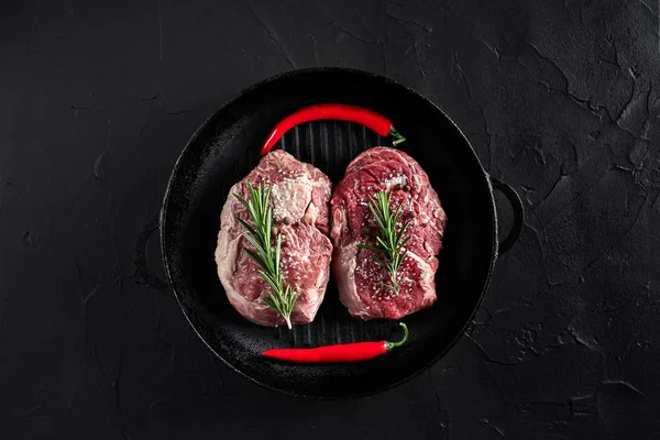 Färsk rå kött. Biff oxfilé och två marmorerat nötköttsbiffar ombord grill pan och stekning med kryddningen, svart bakgrund ovanifrån. — Stockfoto