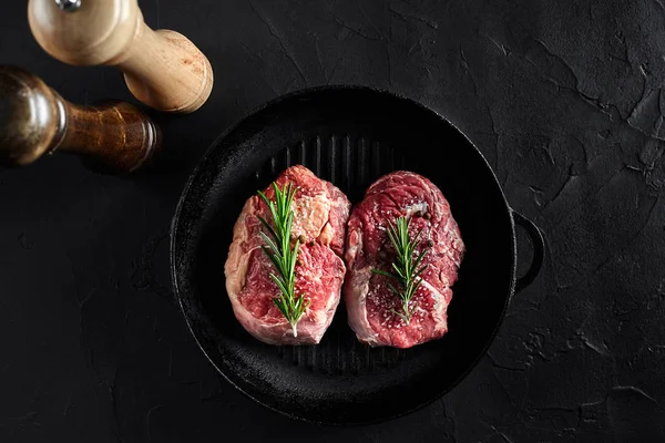 Färsk rå kött. Biff oxfilé och två marmorerat nötköttsbiffar ombord grill pan och stekning med kryddningen, svart bakgrund ovanifrån. — Stockfoto